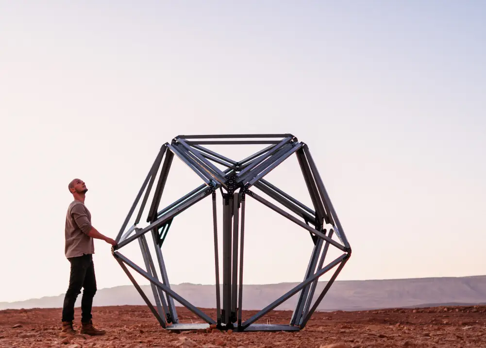 Sebastian standing next to a metal structure which is part of an unfolding habitat in an orange desert