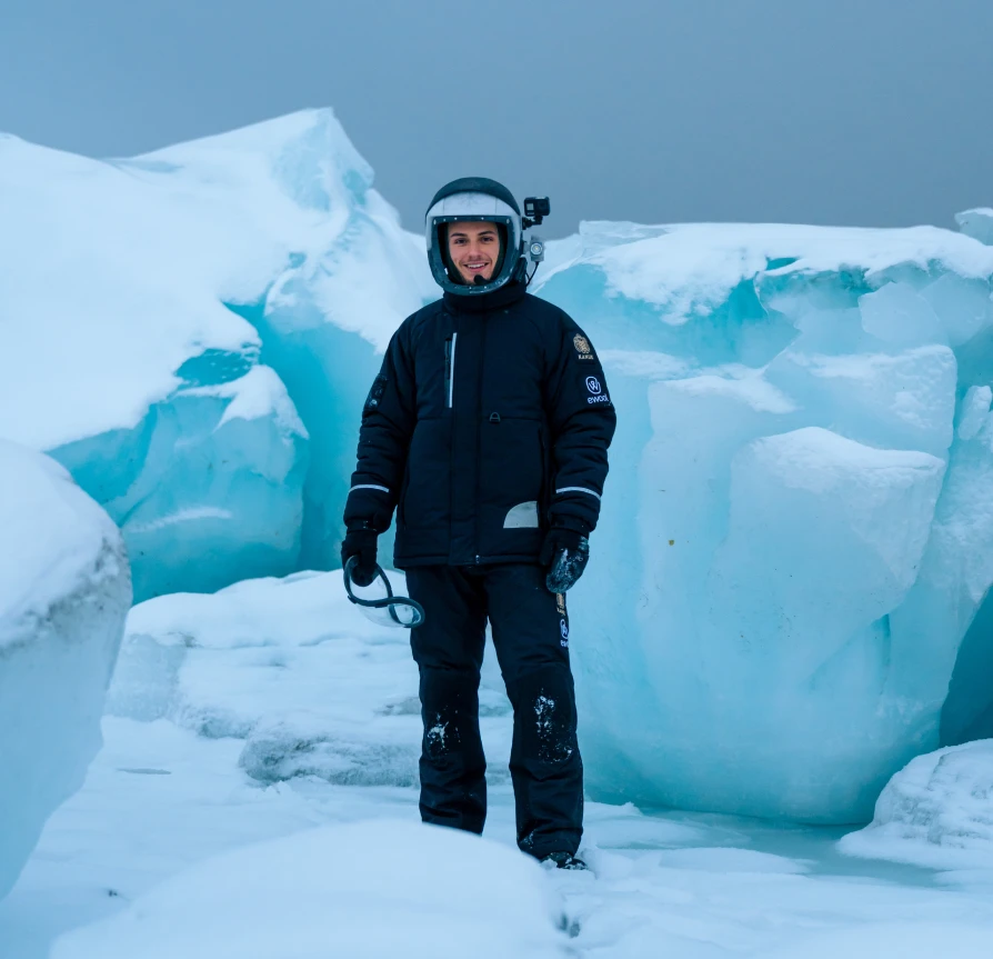 Sebastian Aristotelis standing in his analog space suit among blue and white ice chunks in a snowy landscape